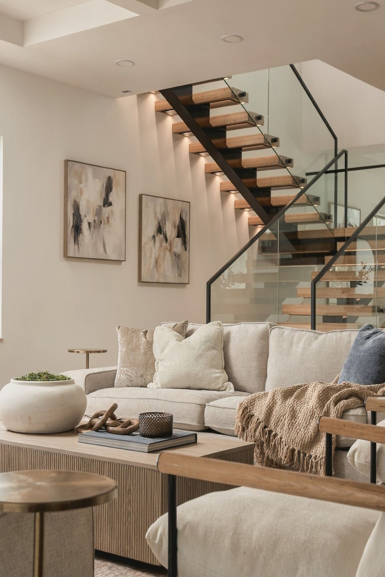 Living room beneath a floating wood staircase with a glass railing