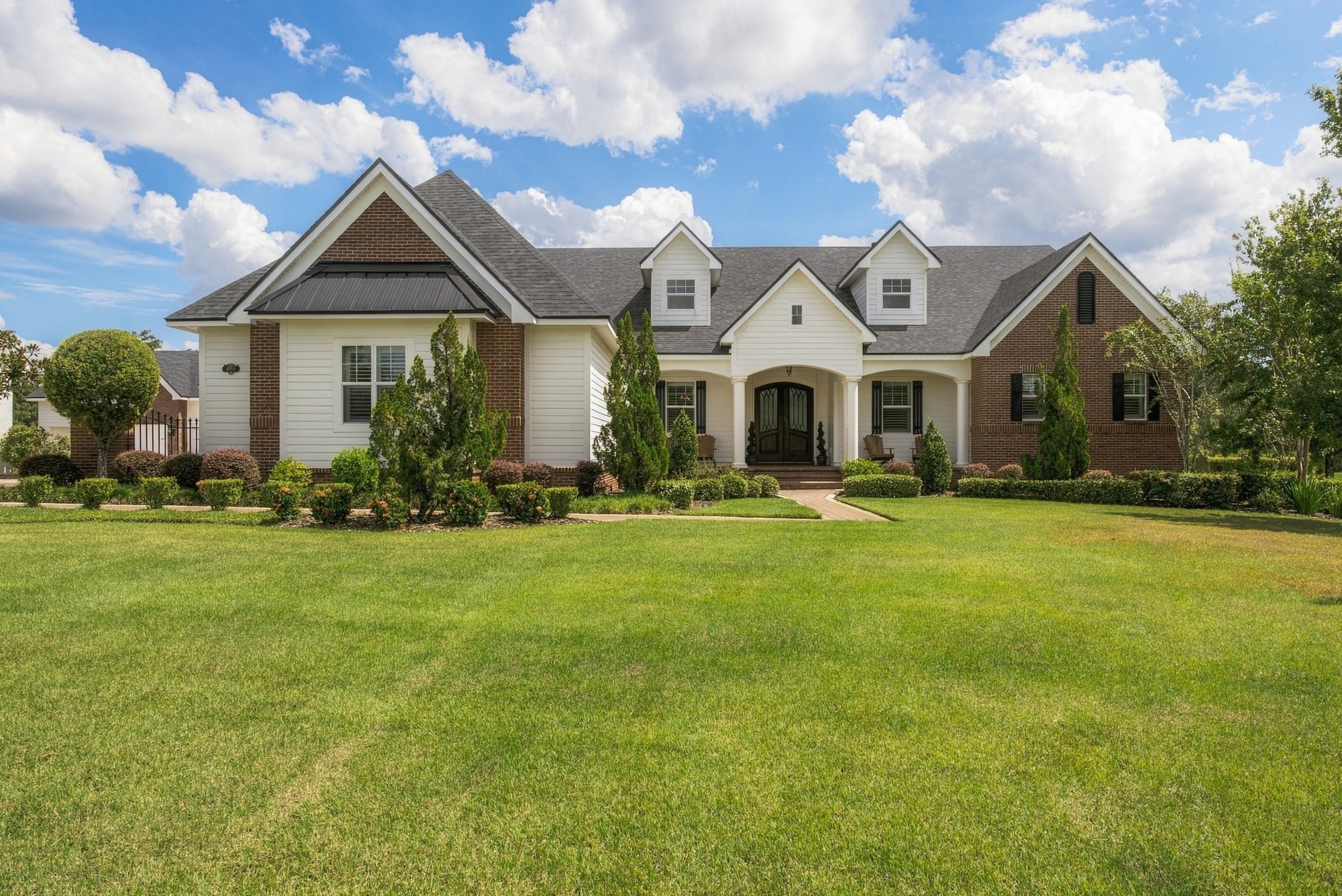 White siding and brick home with an arched porch under a blue sky
