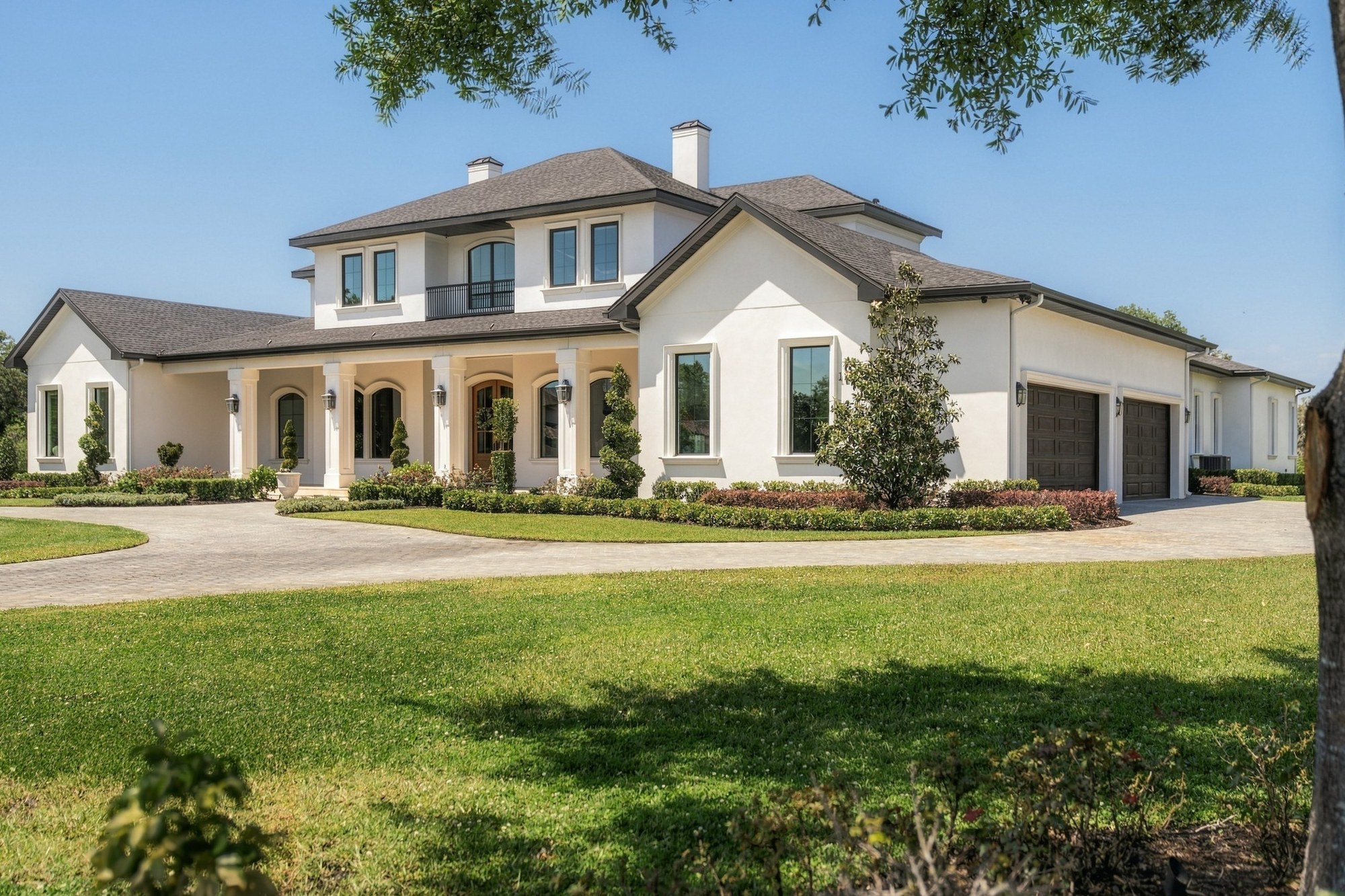 Two-story white stucco home with dark garage doors and a paver drive